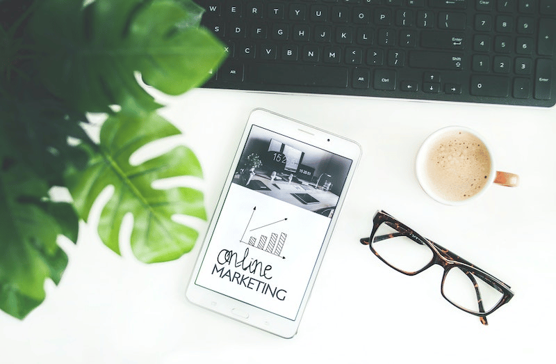 A work desk with glasses, a cup of coffee and a tablet saying online/website marketing