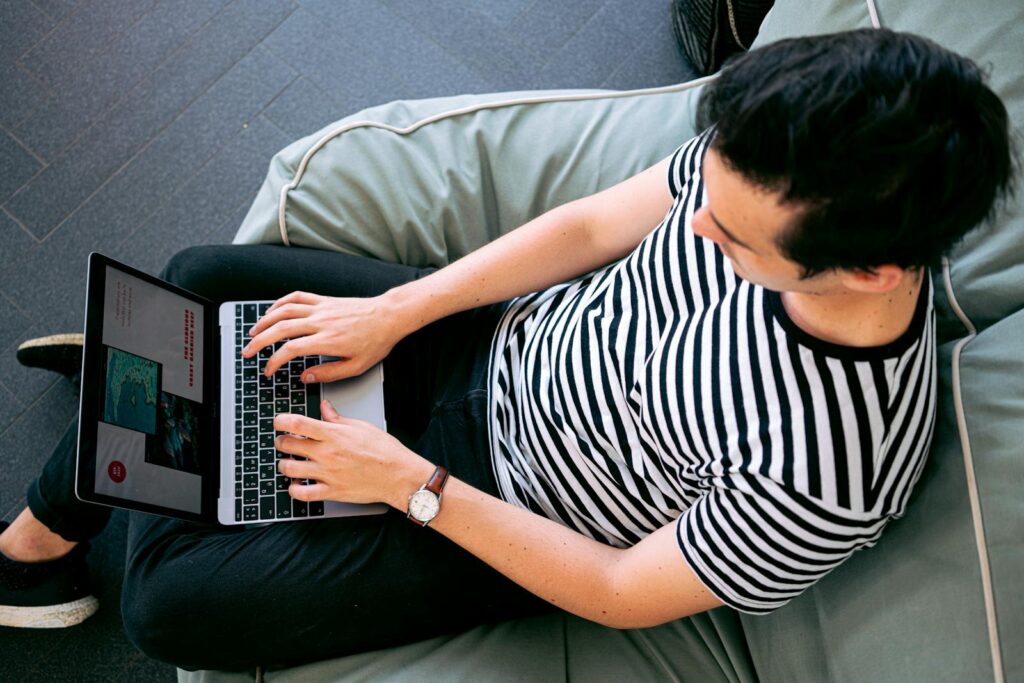 25 Unique Marketing Ideas for Small Business to Boost Growth 8 A man in a striped shirt using a laptop on a bean bag, embodying relaxed productivity.