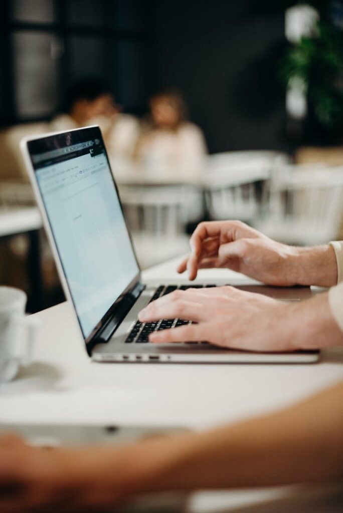 Best Email Hosting for Small Business Success in 2025 9 Close-up of hands typing on a laptop in a cozy indoor cafe setting.