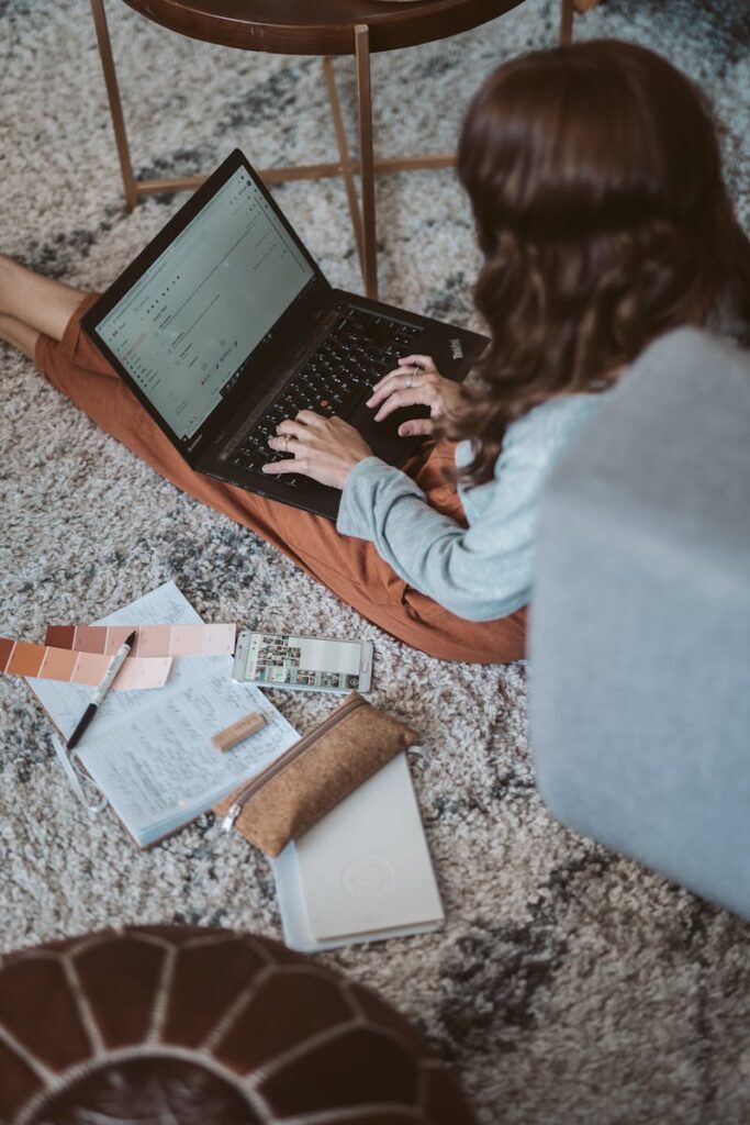Best Email Hosting for Small Business Success in 2025 12 Woman working on her laptop from home, surrounded by design elements on the floor.