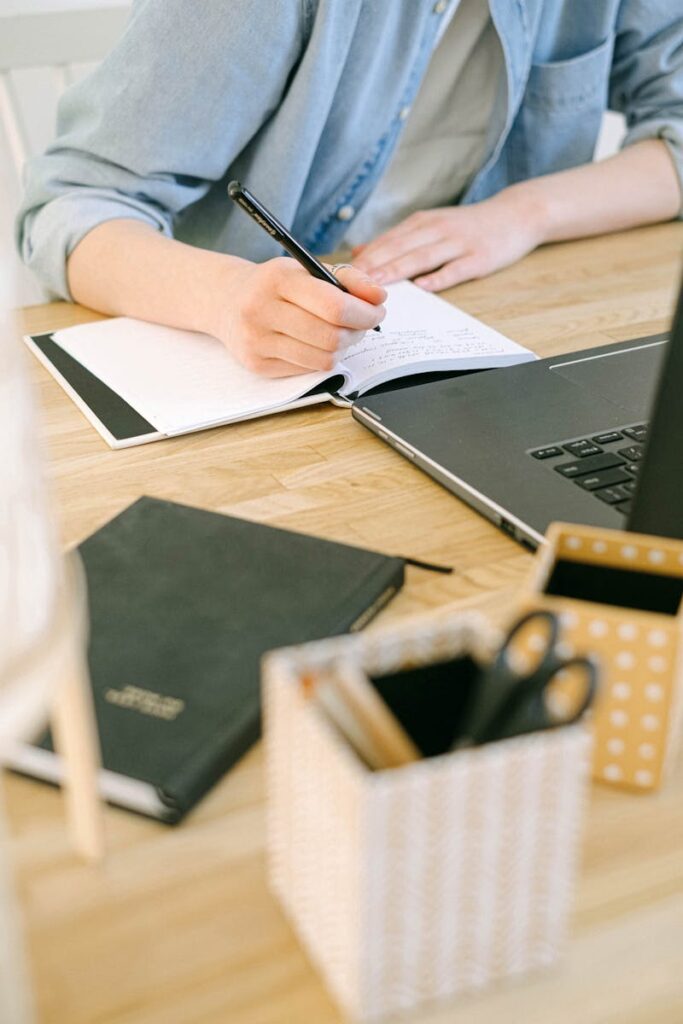 Best Email Hosting for Small Business Success in 2025 13 Adult writing notes on a notebook while working on a laptop in a cozy home office environment.