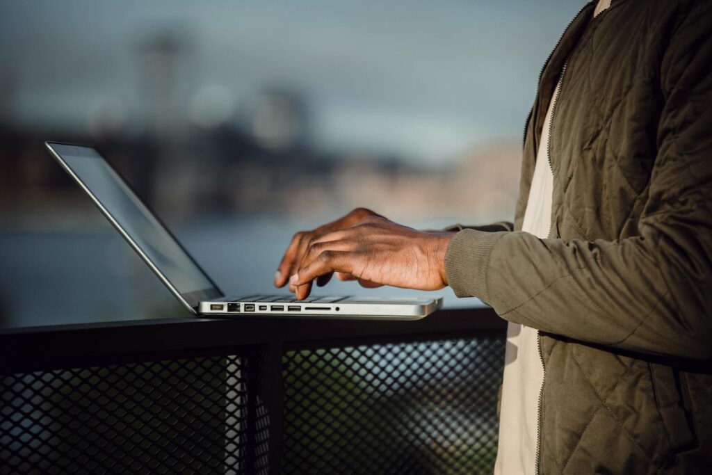 25 Unique Marketing Ideas for Small Business to Boost Growth 9 Man working on a laptop outdoors with city skyline background.