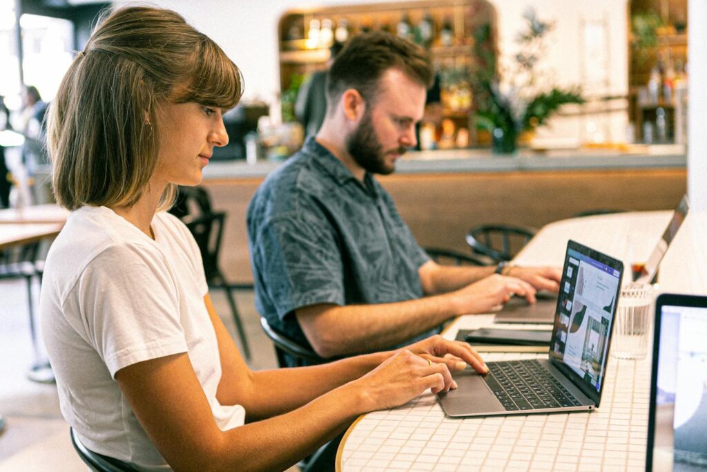 Guide to Marketing Consultants and Priceless Consulting 10 Two young professionals working on laptops in a modern cafe setting.