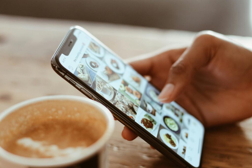 Navigating Social Media Law in 2025 8 Hand browsing social media photos on a smartphone next to a cup of coffee indoors.