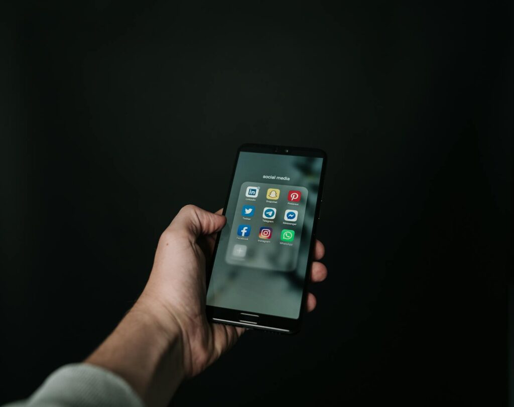 Social Media Consultant: Your Complete Guide to Success 10 Close-up of a hand holding a smartphone displaying various social media app icons on a dark background.