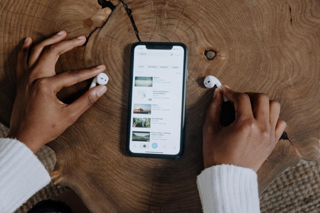 The Complete Social Media Audit Guide for Small Businesses 7 Hands interacting with smartphone and earbuds on a rustic wooden table, highlighting modern technology.