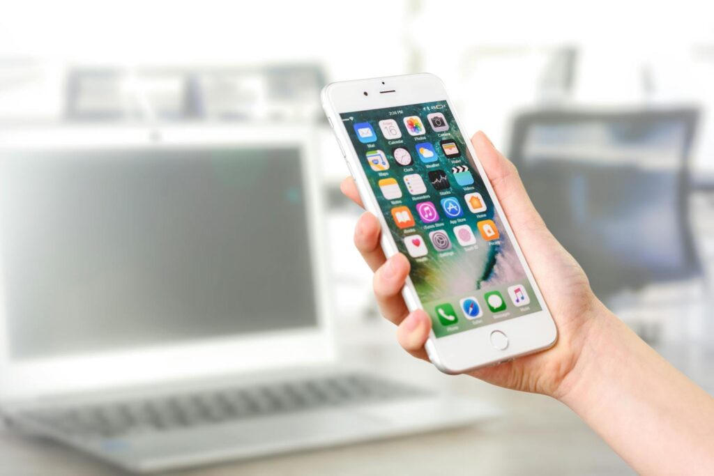 Decoding Social Media Marketing Packages: Your Complete Guide 10 Close-up view of a smartphone displaying apps, held by a hand, with a blurred laptop in the background.