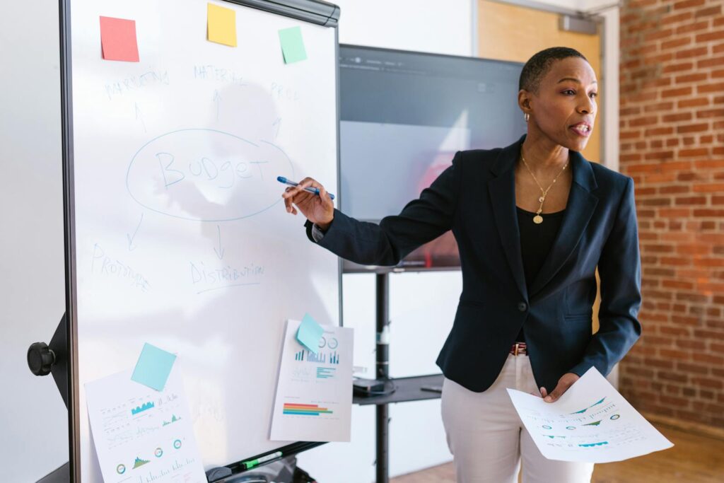 What Does a Social Media Manager Do—and Why Your Business Needs One 4 Professional businesswoman explaining budget strategy on a whiteboard during a meeting.