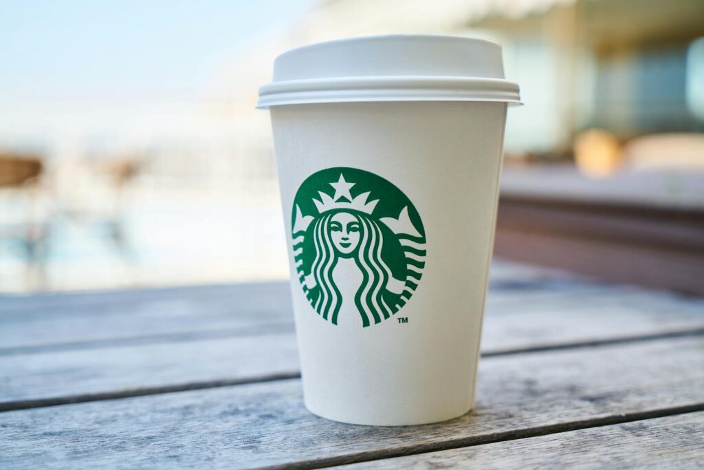 Branding Strategies: How to Build a Memorable and Profitable Brand 4 A disposable coffee cup with a lid outdoors on a wooden table, featuring a popular global logo.
